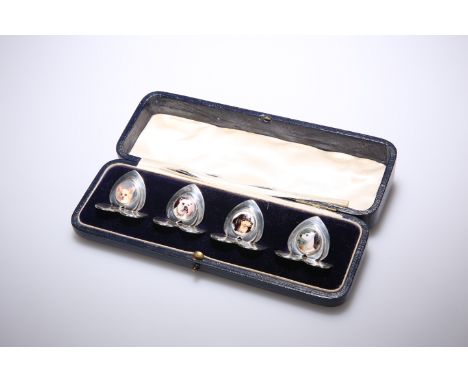 A SET OF FOUR EDWARD VII SILVER AND ENAMEL PLACE CARD HOLDERS, BY SAMPSON MORDAN AND CO., CHESTER, 1907, each on heart-shaped