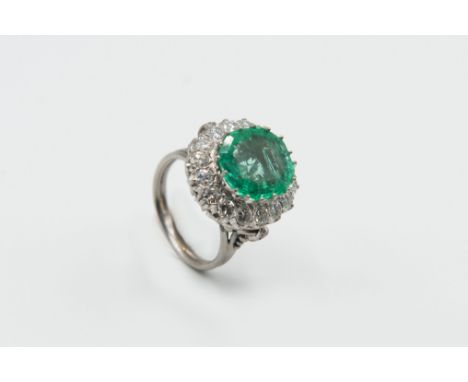 AN EMERALD AND DIAMOND CLUSTER RING, the large oval cut emerald claw set, raised within a surround of sixteen brilliant cut d