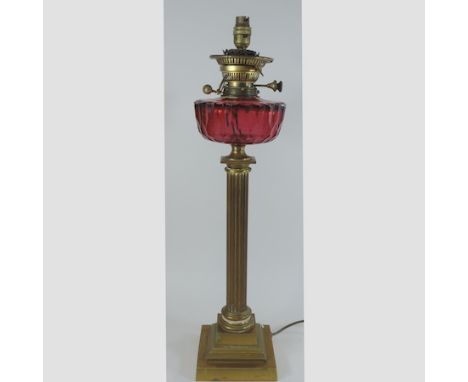 A brass oil lamp, with a cranberry glass reservoir, converted to a table lamp, 67cm tall overall