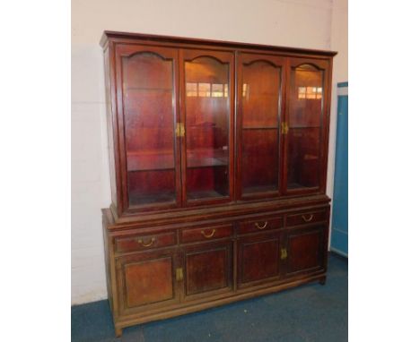 A Chinese hardwood cupboard bookcase, the outswept pediment over four doors enclosing glass shelves, over four frieze drawers