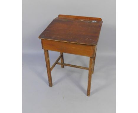 An early 20thC stained pine child's school desk, with a pen recess and inkwell, sloping lid, raised on square legs united by 