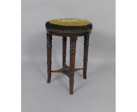 A Victorian mahogany circular piano stool, with floral tapestry woolwork seat, raised on turned legs united by an under tier.