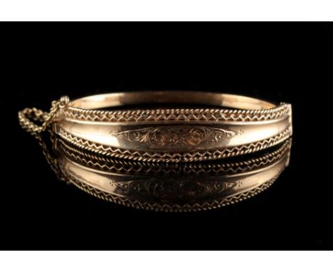 Property of a lady - a 9ct gold hinged bangle, with engraved foliate decoration &amp; pierced borders, with safety chain (see
