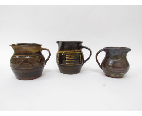 Three studio pottery jugs in the Winchcombe style, two unmarked, one with indistinct seal. Largest 12cm high (3)
