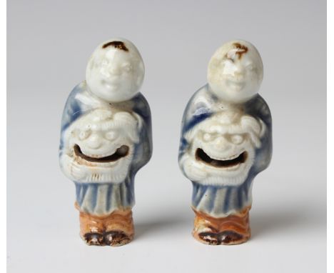 Two rare Japanese Hirado porcelain netsuke rattles, Edo period, each modelled as a Chinese boy holding a lion mask and wearin