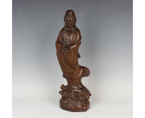A Chinese carved hardwood figure of Guanyin, 20th century, modelled standing wearing a long robe on a carved scroll base, hei