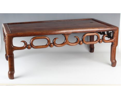 A Chinese hardwood low table, early 20th century, the rectangular panelled top above a carved and pierced scroll frieze, on s