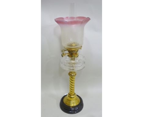 A LATE VICTORIAN OIL LAMP, having brass spiral twist column supports, clear glass reservoir, an etched cranberry tinted shade