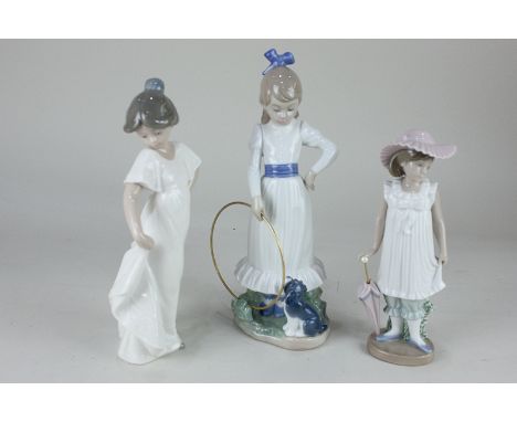 Three Nao figures to include a young girl holding a metal hoop beside a puppy, 24.5cm, and a girl wearing a pink hat and hold