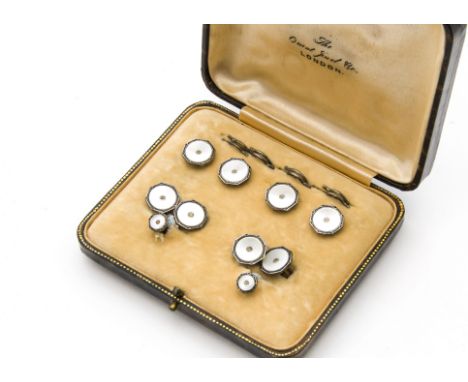 An Art Deco silver and mother of pearl dress stud and cufflink set, in a fitted box, each heightened with blue enamel rims an