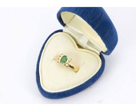 A modern 18ct gold emerald and diamond ring, oval green stone in four claws flanked by three brilliant cuts, with valuation c