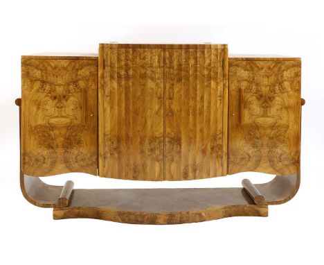 An Art Deco burr walnut serpentine sideboard,the raised central cupboard, with a fluted bow front, opening to reveal a mirror