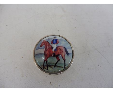 A circular silver and enamel topped pill pot, the lid decorated with a jockey cantering on his horse, marked .925 to the base
