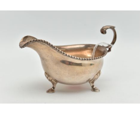 A MID 20TH CENTURY SILVER GRAVY BOAT, polished form, gadrooned rim, fitted with a scroll handle, raised on three hoof feet wi