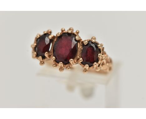 A 9CT GOLD THREE STONE RING, claw set with three oval cut garnets, applied bead work surround, textured scroll detailed shoul