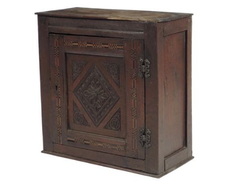 An oak hanging wall cupboard, the panelled door carved with leaves and flowers with fruitwood and ebonized parquetry bands, t