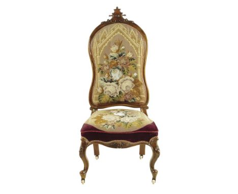 A Victorian walnut nursing chair, with needle and beadwork upholstery depicting Gothic buildings and flowers on carved cabrio