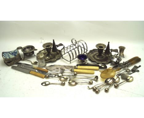 A collection of silver plate and metalware, including a candlestick, flatware, toast rack, condiment pots and more, some exam