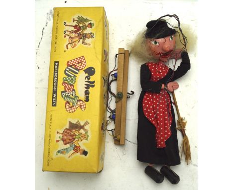 A Pelham puppet of a witch carrying a broom, dressed in a black dress with red and white spotted scarf, in original bix, heig