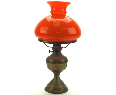 An early/mid 20th century brass oil lamp, adorned with an orange glass shade, measuring approximately 45cm high