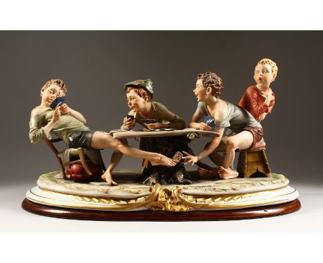 A VERY GOOD CAPODIMONTE PORCELAIN GROUP by MERLI. Four boys playing cards, two cheating, on a wooden base. 53cms long.