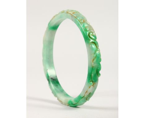 A LARGE CHINESE GREEN AND WHITE JADE BANGLE, with carved decoration. 10.5cms diameter.