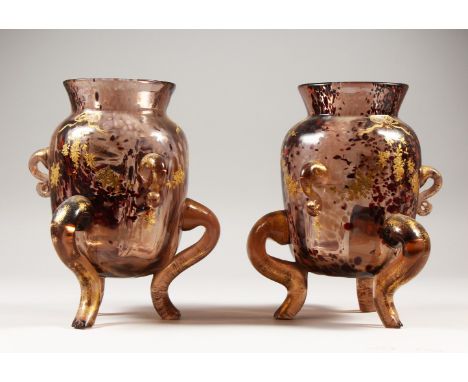 AN UNUSUAL PAIR OF CONTINENTAL MOTTLED RUBY VASES, with gilt decoration, on three curving legs. 23cms high.