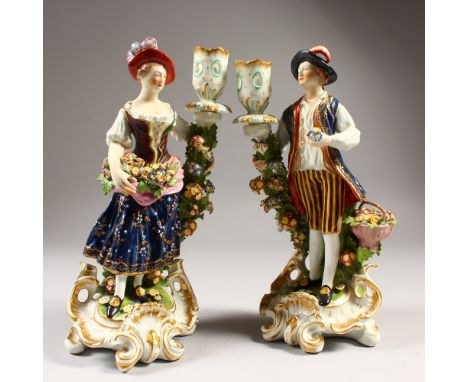 A PAIR OF DERBY CANDLESTICK FIGURES, gallant and lady in rich garb, each with a candlestick encrusted with flowers, the base 