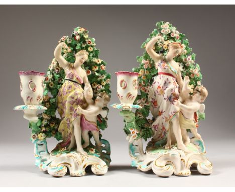 A GOOD PAIR OF DERBY CANDLESTICK GROUPS, classical lady with a cupid standing before a bocage, on a scrolled base. 20cms high