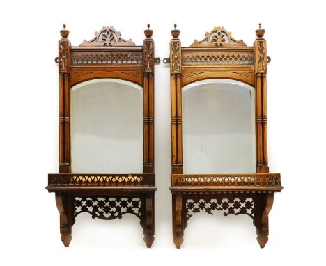 A pair of Edwardian walnut wall mirrors,in the Gothic taste, each supporting a shelf with a pierced gallery, below a bevelled