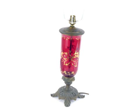 An early 20thC ruby glass table lamp, the shaped lamp with gilt painted decoration, on a leaf and flower moulded foot, 61cm h