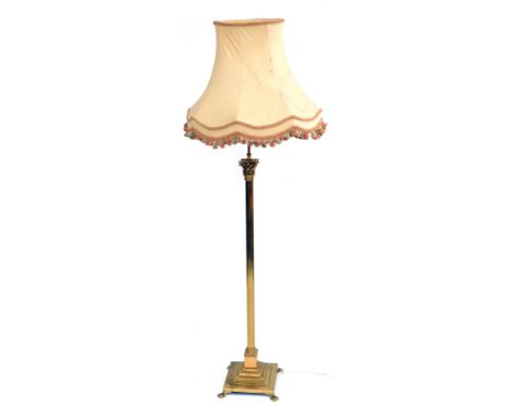 A brass Corinthian column standard lamp, raised on a stepped square base on lion's paw feet, with a cream coloured shade, 178