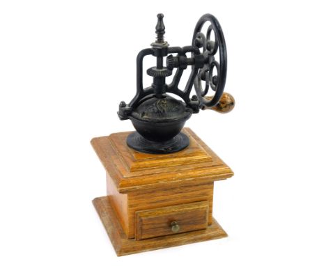 A French vintage cast iron coffee grinder, with a wheel turning handle, raised on an oak base with single drawer, 28cm high.