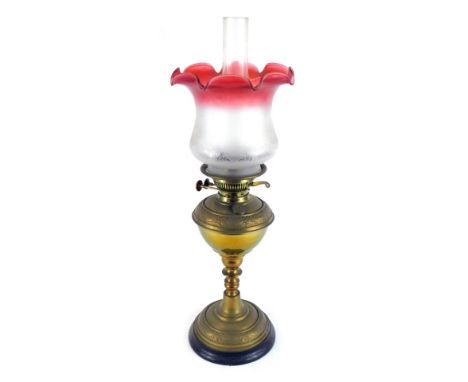 A brass oil lamp, with a cranberry frosted glass shade, and chimney, on brass embossed body, on an ebonised circular foot, 67