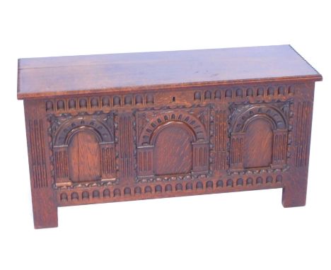 A 17thC style oak blanket box, the hinged lid opening to reveal a vacant interior, the triple panel front carved with arched 