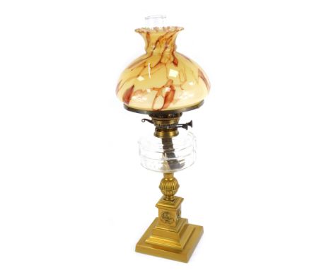 An early 20thC brass oil lamp, with a marbled effect orange and red shade, with funnel, glass reservoir, on a square set bras