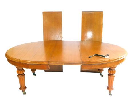 A Victorian light oak wind out dining table, with three additional leaves, raised on fluted and turned legs, brass capped on 