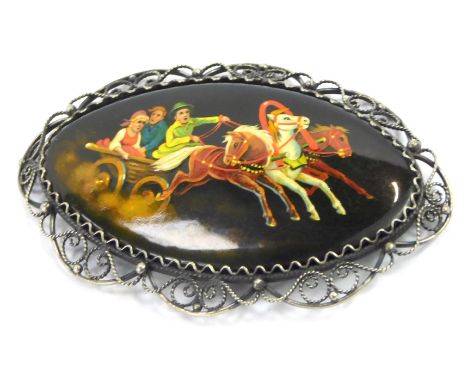 A Russian hand painted brooch, the panel depicting horse and troika, with figures, with white metal filigree scroll border, b