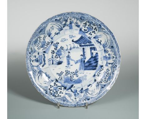 A Kangxi period dish, painted with a couple holding hands outside a pavillion, within lappet decorated rim with figures, flow