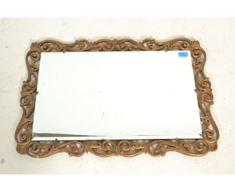 A vintage 20th Century decorative gilt framed mirror of pierced scroll decoration having a rectangular bevelled edge mirrored