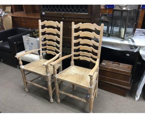 A pairvof lined oak ladder back open arm chairs with woven rush seats.
