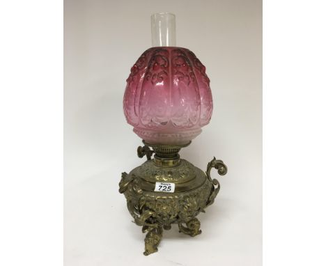A Quality Victorian brass oil lamp with an ornate base with scroll supports and raised masks with an etched cranberry shade.
