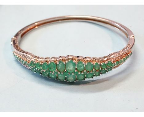 An emerald and silver hinged bangle claw set two rows of graduated oval emeralds with round cuts between, in plain tapered mo