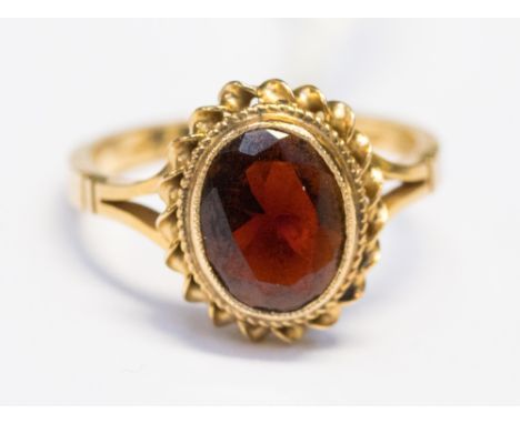 A 9ct gold and garnet dress ring, set with an oval garnet with rope edge surround, size J, with a total gross weight of appro