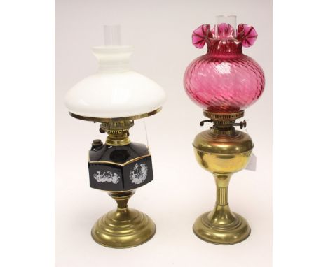  Two oil lamps, brass based ceramic oil reserve, Cranberry coloured globe and opaque glass globe (2) 