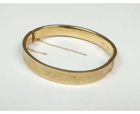 A 9ct gold hallow hinged bangle, with attached safety chain, weight 12.3g (at fault)