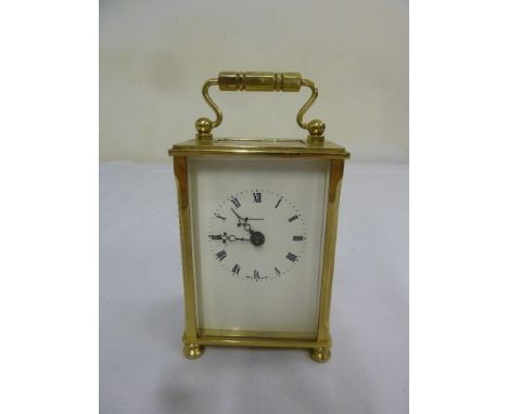 Gilt metal carriage clock with enamel dial, Roman numerals and central carrying handle on four bun feet