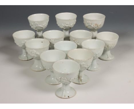 China, set van dertien blanc-de-chine wijnkopjes, 18e eeuw, elk op hoge voet en gemodelleerd met prunus (chips, haarlijnen) [
