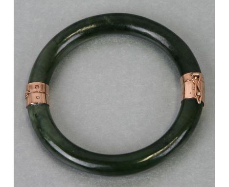 A yellow metal mounted (tests as gold) opening dark green figured jade bangle, 7.5cms dimeter.