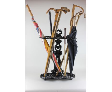 A black painted cast iron stick stand with two divisions and an assortment of walking sticks and umbrellas